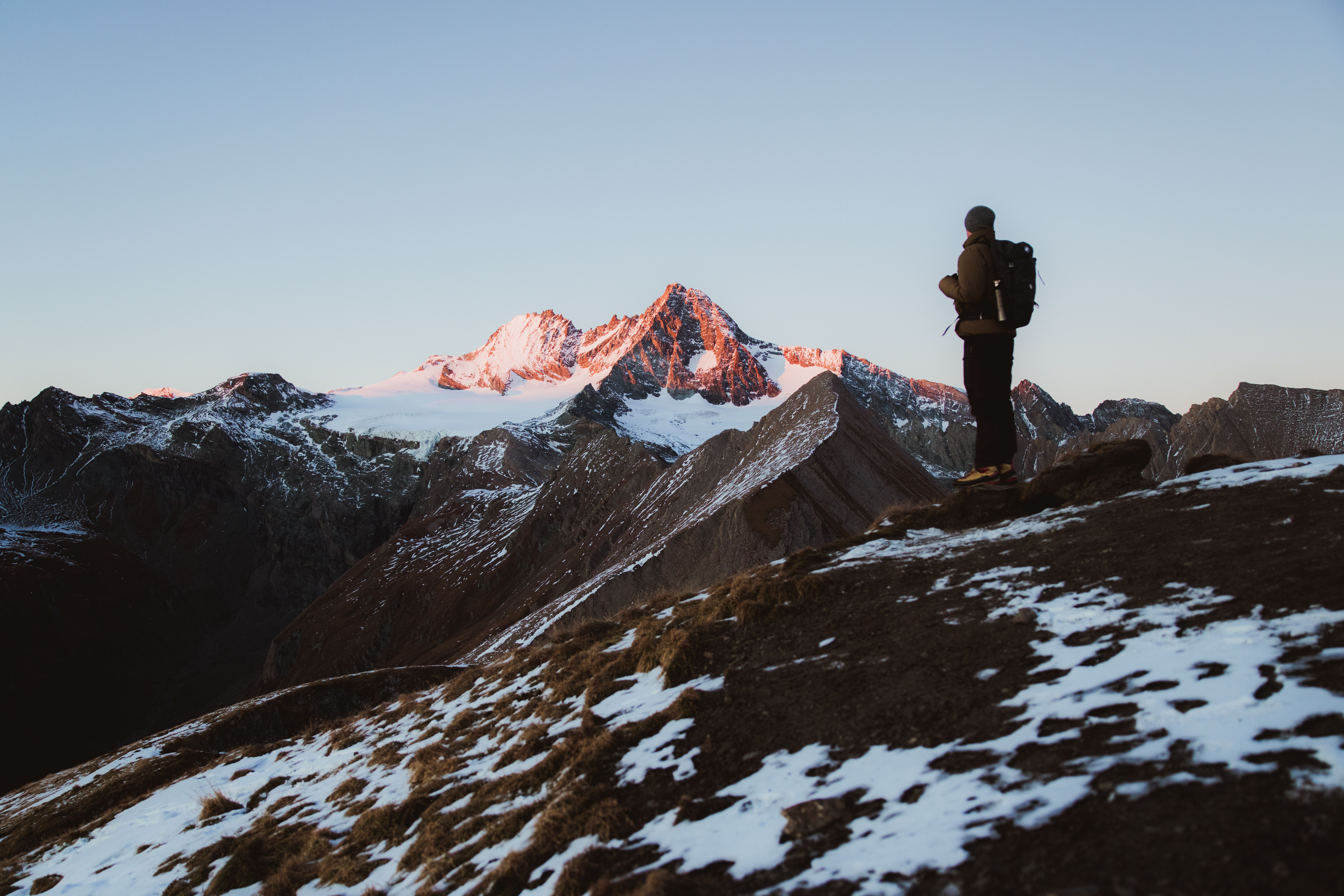 Mann auf einem Gipfel im Vordergrund, im Hintergrund der angestrahlte Großglockner, Abenddämmerung