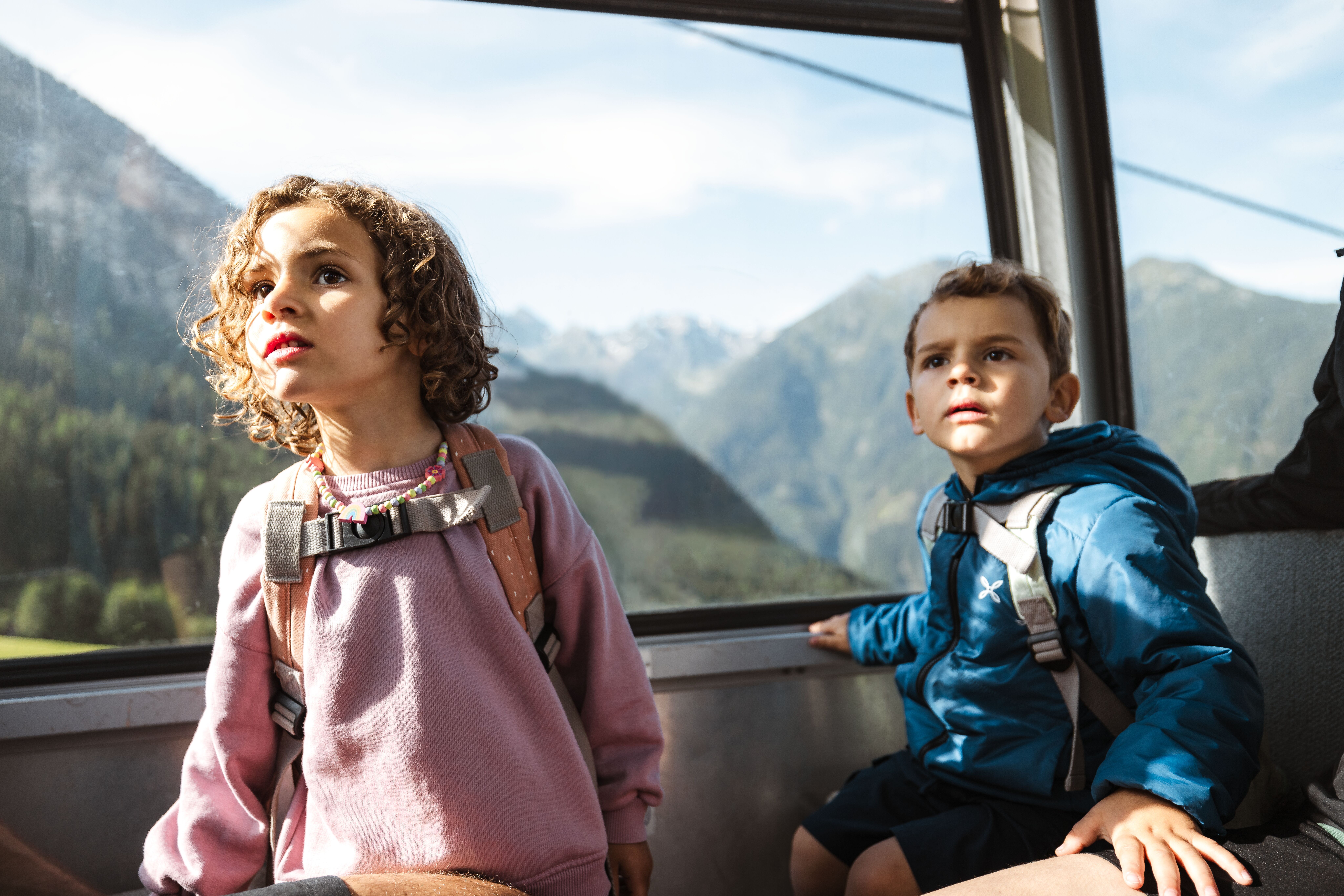 zwei Kinder, ein junge und ein Mädchen schauen aus einer Gondel in die Bergwelt, Sommerbergbahn mit der Familie in Jerzens am Hochzeiger, Pitztal 